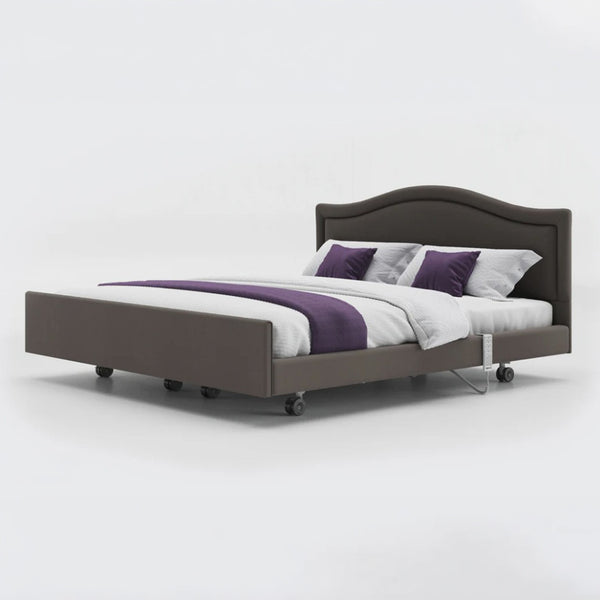 Dual profiling bed with leatherette headboard, white bedding, and wheels on the base, front view.