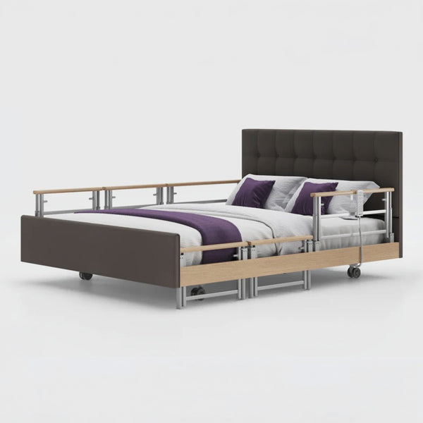 Opera Beds Signature Comfort Plus Dual Profiling Bed with drop side rails, wheels, and white, grey, and purple bedding, front view.