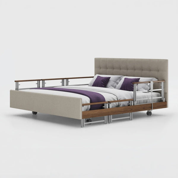Opera Beds Signature Comfort Plus Dual Profiling Bed with drop side rails, wheels, and purple-white bedding, front view.