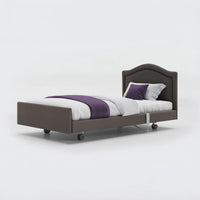 Profiling bed with white bedding, purple blanket and two pillows on a grey frame, leatherette finish, front view.
