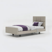 Opera Beds Signature Comfort Profiling Bed with wheels, white bedding and purple pillows on a white background, front view.