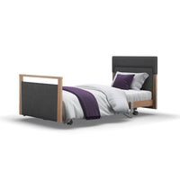 Opera Beds Signature Upholstered Profiling Bed with wood accents, white bedding, and purple accessories on white background, front view.