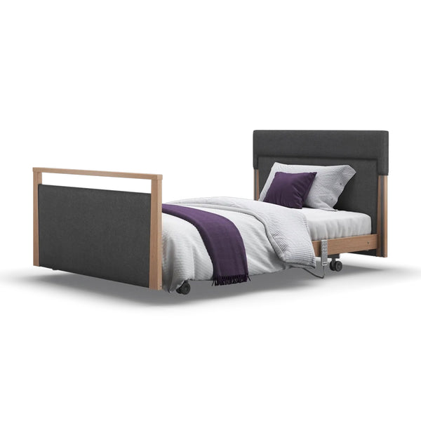 Opera Beds Signature Upholstered Profiling Bed with wood accents, white bedding, purple blanket, two pillows on wheels, front view.