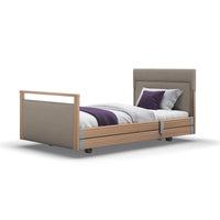 Opera Beds Signature Profiling Bed with linen upholstery, wooden frame, headboard, white bedding, purple blanket, on wheels, front view.