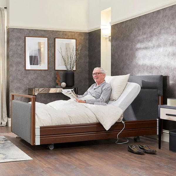 Elderly man reading a newspaper in an Opera Beds Signature Upholstered Profiling Bed in a modern bedroom, in use.