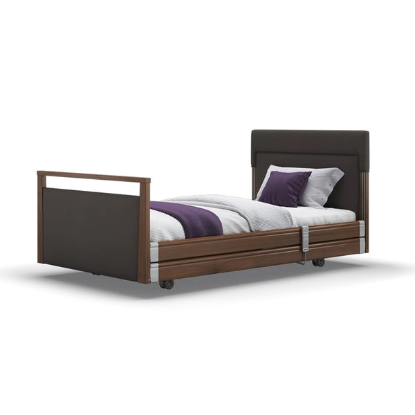 Upholstered profiling bed with wheels, white bedding, purple throw, and two pillows, side view.