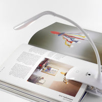 The Daylight Company Smart Clip-On Lamp lighting an open book with text and images on a white surface, in use.