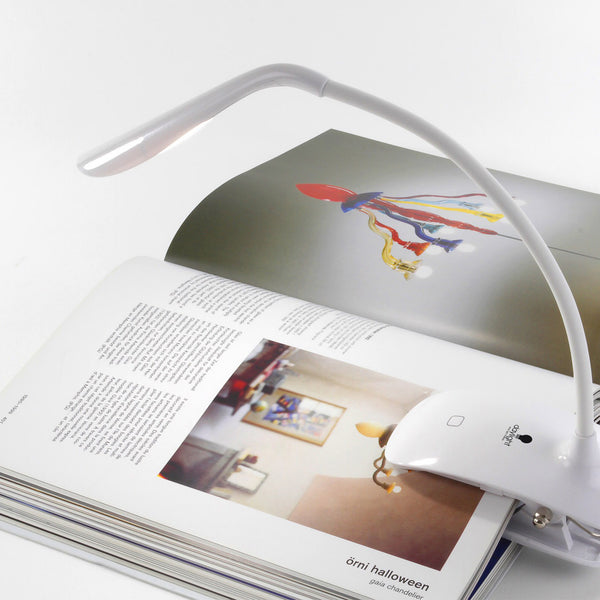 The Daylight Company Smart Clip-On Lamp lighting an open book with text and images on a white surface, in use.