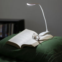 Smart Clip-On Lamp by The Daylight Company lighting an open book and eyeglasses on a pillow, in use view.