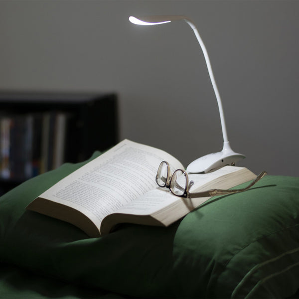 Smart Clip-On Lamp by The Daylight Company lighting an open book and eyeglasses on a pillow, in use view.
