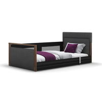 Opera Beds Solo SafeSide Profiling Floor Bed with wood accents, white bedding, purple pillows, and safety rail, side view.