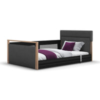 Opera Beds Solo SafeSide upholstered profiling floor bed with wooden accents, white bedding and purple accessories, side view.