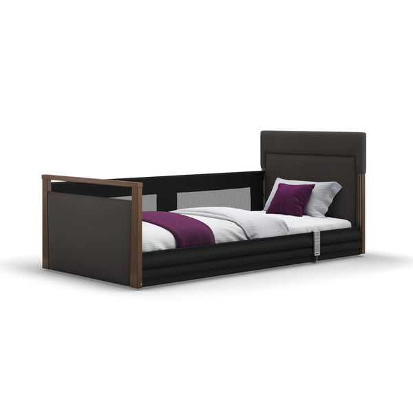 Opera Beds Solo SafeSide Profiling Floor Bed with safety rail, dark frame, white bedding, and purple accent pillow, side view.