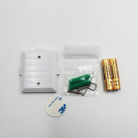 Hearing Products International Sound Sensor Transmitter with 3M adhesive, wall plugs, screws and two AA batteries, overhead view.