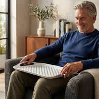 Man in blue sweater sitting in armchair holding Able2 Stayput Anti-Slip Tray with black handles on lap, in use view.