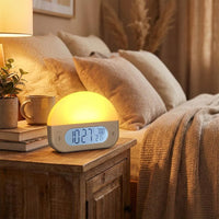 Lifemax Sunrise Alarm Clock on nightstand next to mug and neatly made bed in warm bedroom, side view.