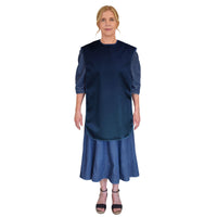 Woman wearing Care Designs Tabard Style Adult Bib over a blue dress and black sandals, white background, front view.