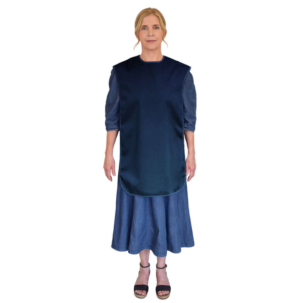 Woman wearing Care Designs Tabard Style Adult Bib over a blue dress and black sandals, white background, front view.