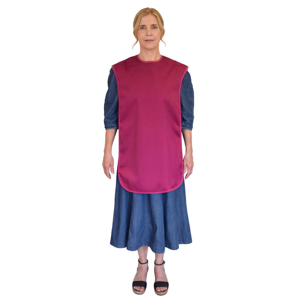 Woman wearing Care Designs Tabard Style Adult Bib over a long denim dress, standing and facing forward, white background, front view.