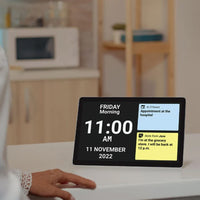 Ravencourt Idem Digital Dementia Clock showing date, time, and reminders on kitchen counter with seniors hand nearby, in use.