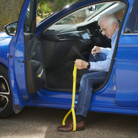 Older man using Helping Hand Leg Up Leg Lifter to assist exiting a blue car, door open, in use view.