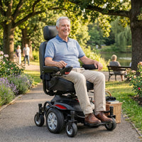 Drive Titan AXS Mid-Wheel Powerchair in use by older man on park path with trees, flowers and people on bench, side view.