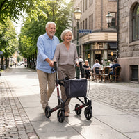 Elderly woman using a Topro Troja 5G Premium Rollator near shops and café, man walking beside her, in use outdoors.