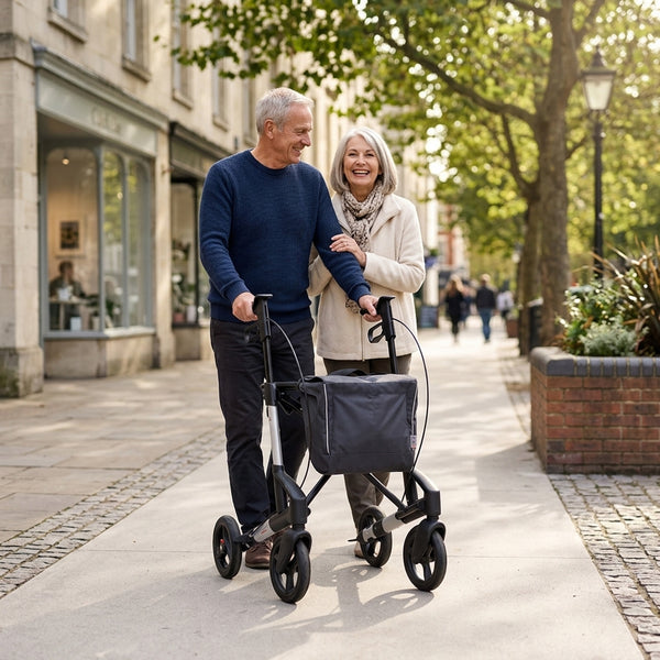 Older couple walking outdoors, one using Topro Troja 5G Premium Rollator for support, trees and shops in background, in use view.