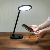 TriSun Therapy Lamp by The Daylight Company with phone charging via USB port on a wooden table, in use.
