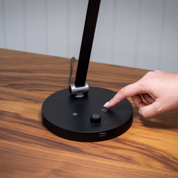 Hand pressing power button on The Daylight Company TriSun Therapy Lamp with adjustable brightness, on a wooden surface, close-up.