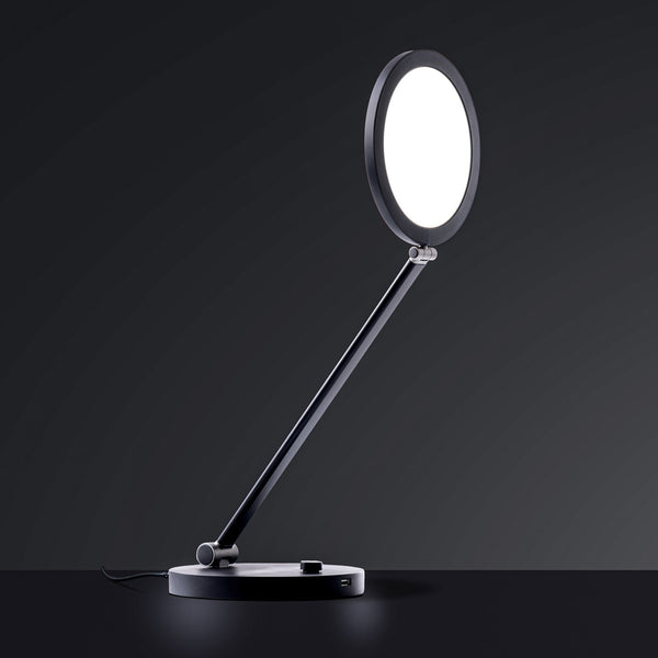 The Daylight Company TriSun Therapy Lamp with circular light and adjustable arm, dark background, angled front view.