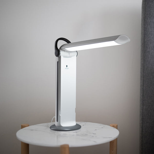 Twist 2 Portable Lamp with curved arm on round marble table, light wall background, side view.