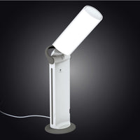 The Daylight Company Twist 2 Portable Lamp, foldable with a round base, shown against a dark background, front view.