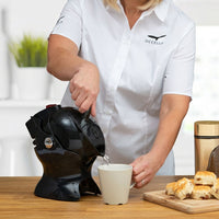 Pouring hot water from a Uccello Designs Uccello Kettle into a white mug on a wooden table with pastries and jar, in use view.