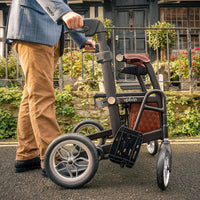 Person outdoors with Able2 Uplivin Glide 2-in-1 Rollator and Wheelchair, in use rear angle.