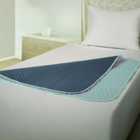 Green waterproof washable bed pad on white-sheeted bed with pillow, pad partly folded back, front view.