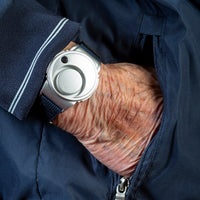 Solon Security Wrist Alarm worn on an elderly wrist, hand inside a jacket pocket, in use close-up.