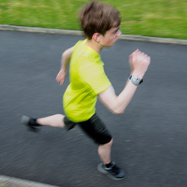 Boy jogging on a paved path wearing Solon Security Wrist Alarm, motion blur shows movement, in use view.